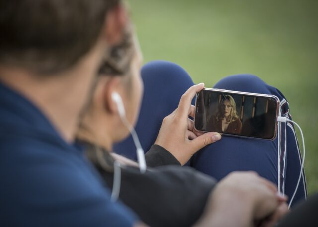Two people listen with earbuds while watching a video on a mobile phone.